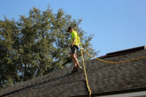 A homeowner inspects roof shingles and cleared gutters on a gabled house beneath dark storm clouds.